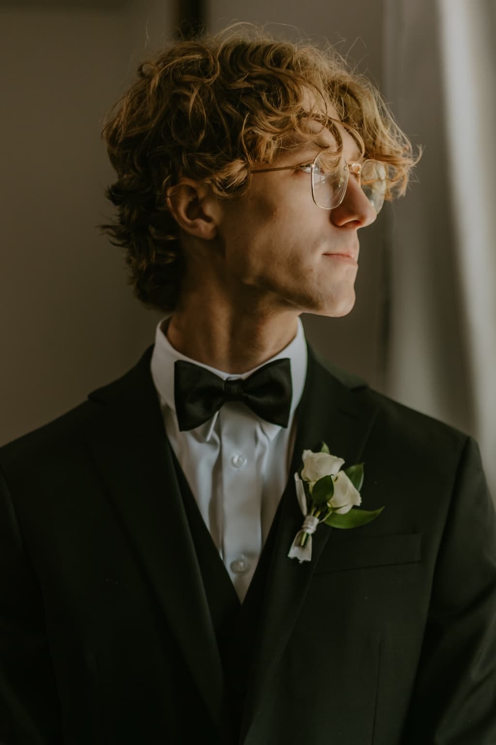 Groom in a black tuxedo standing by a window before the wedding ceremony
