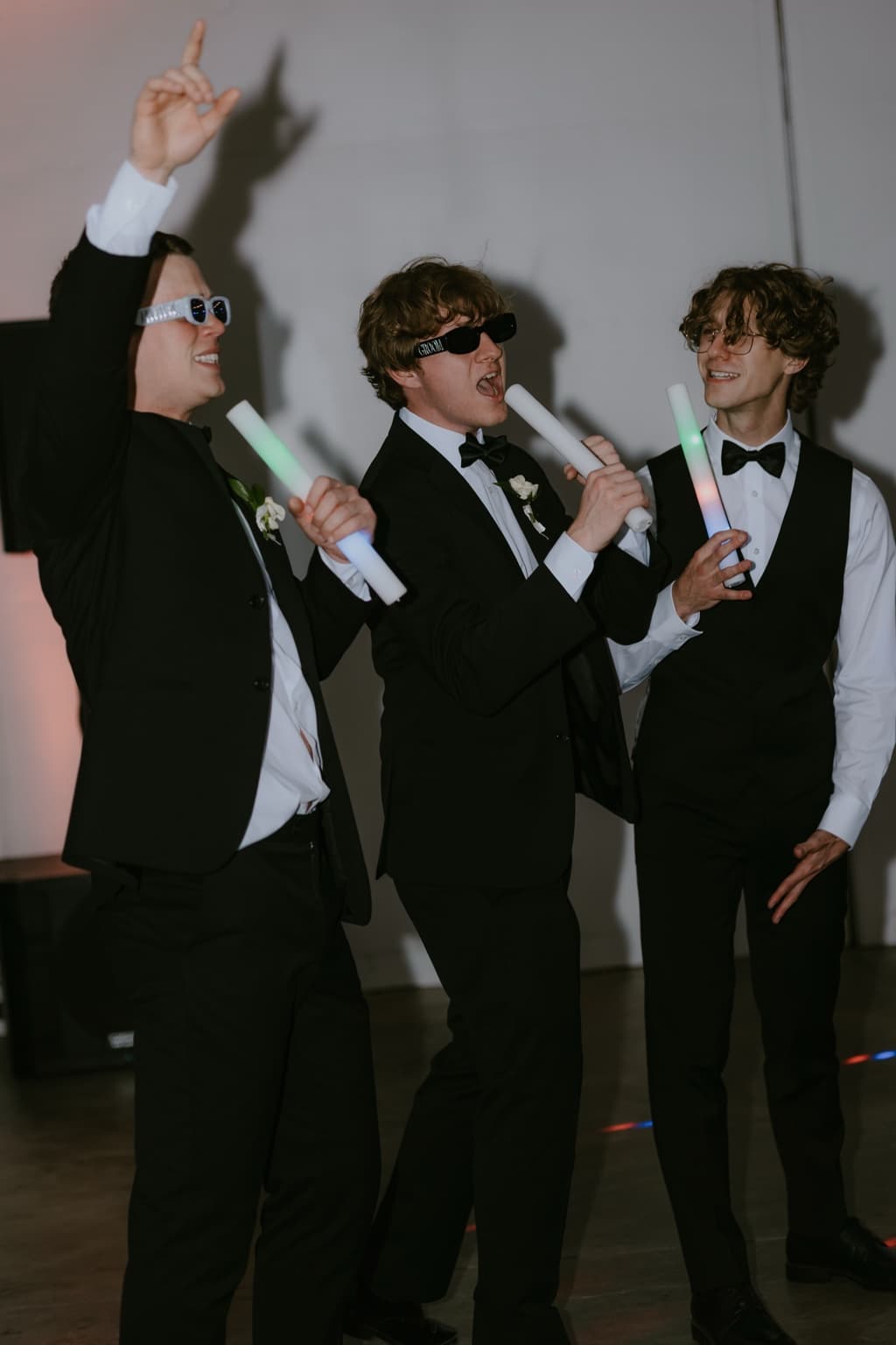 Groomsmen celebrating with glow sticks and playful sunglasses on the dance floor
