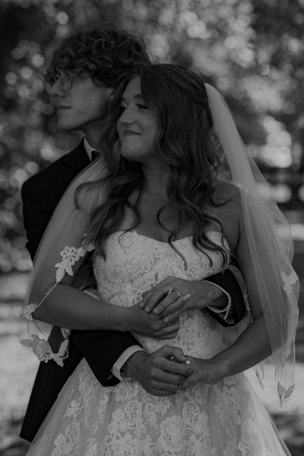 Black-and-white portrait of newlyweds embracing beneath the bride's veil