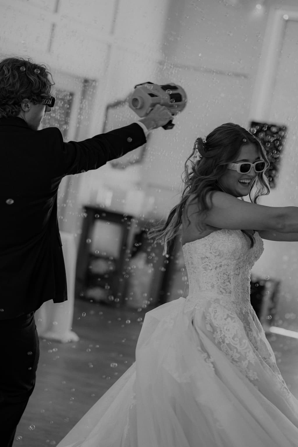 Black-and-white photo of the bride and groom dancing through bubbles at the reception