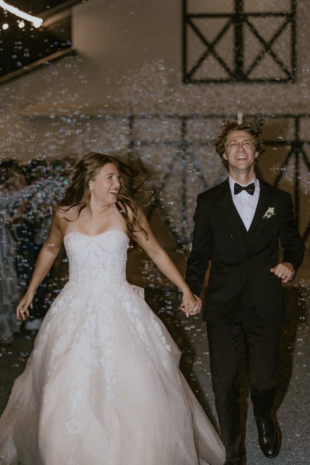 Bride and groom laughing as they walk through bubbles after their reception