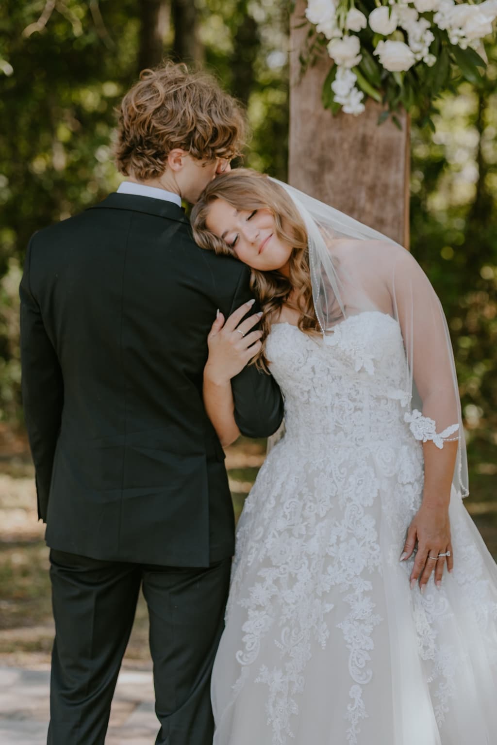 Bride resting her head on the groom beneath the ceremony cross