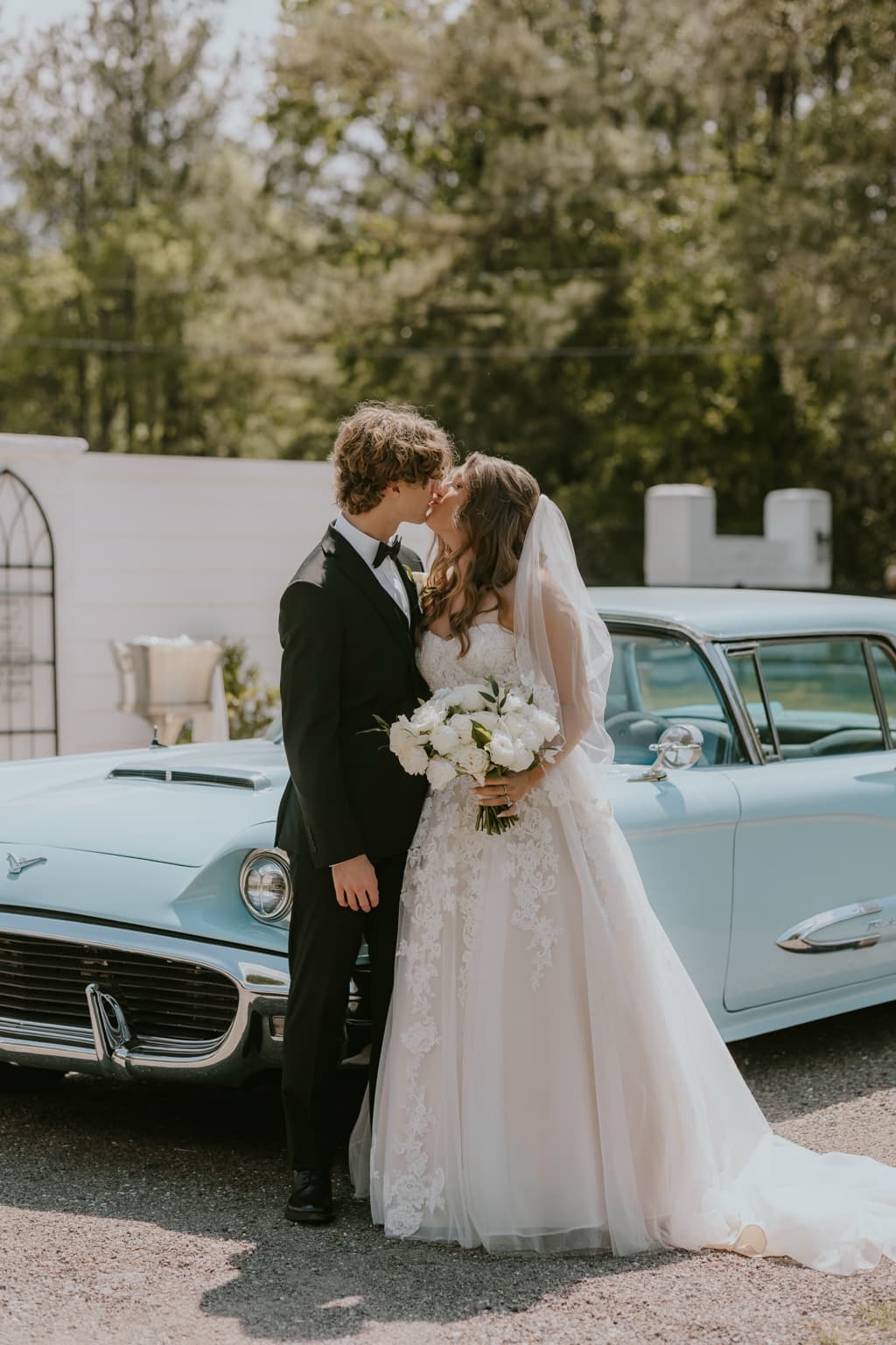 Bride and groom kissing beside a light blue vintage wedding car