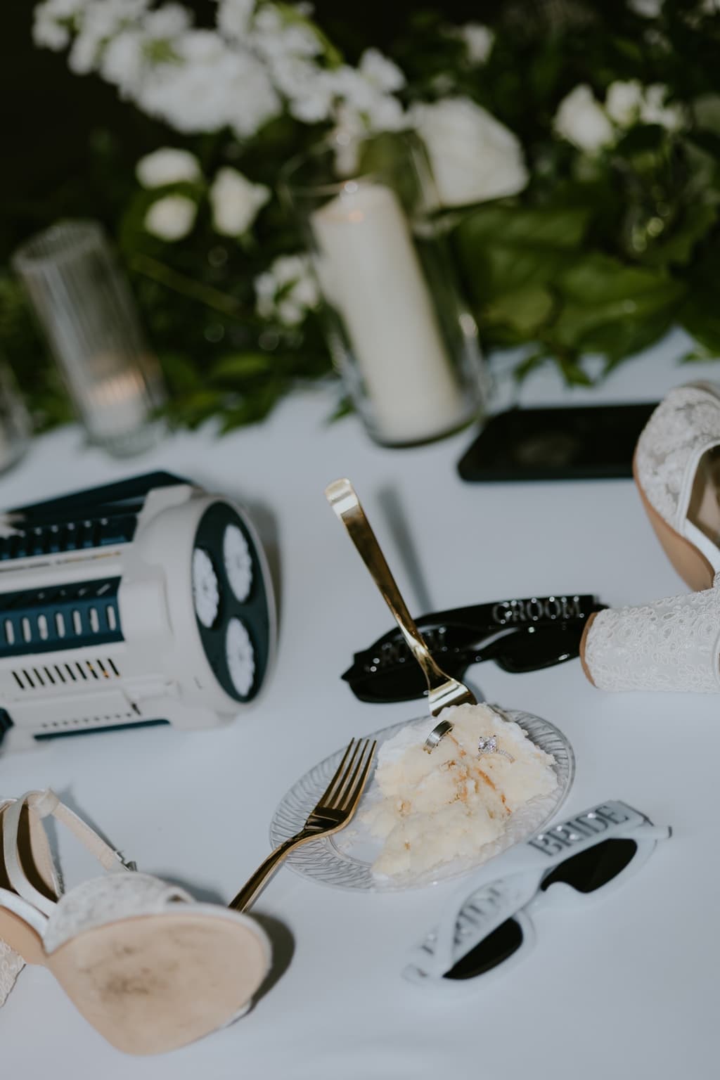 Wedding cake slice with rings, gold flatware, bridal shoes, and reception accessories